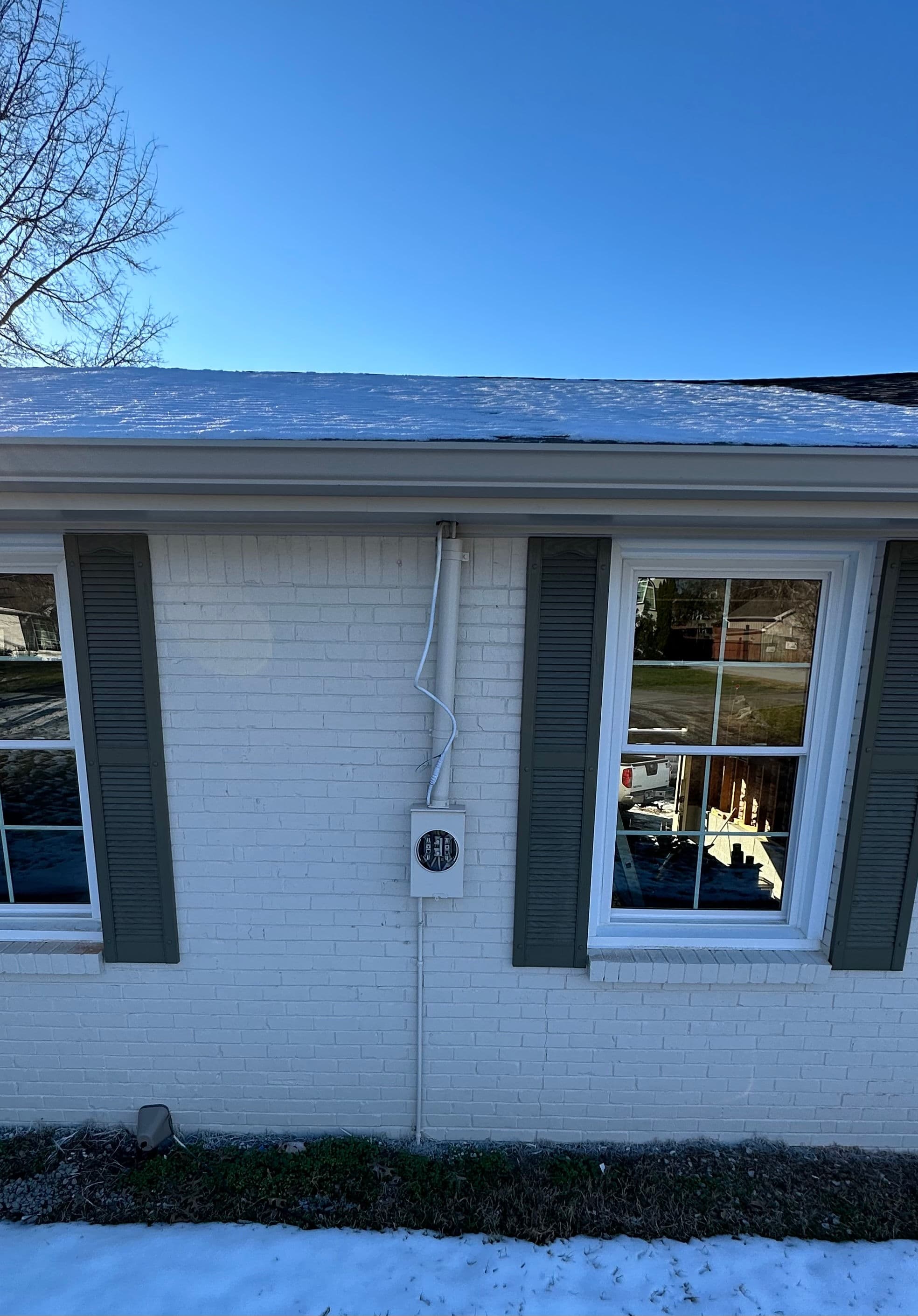 Exterior view of a house with snow on the roof and a utility meter on the side wall.