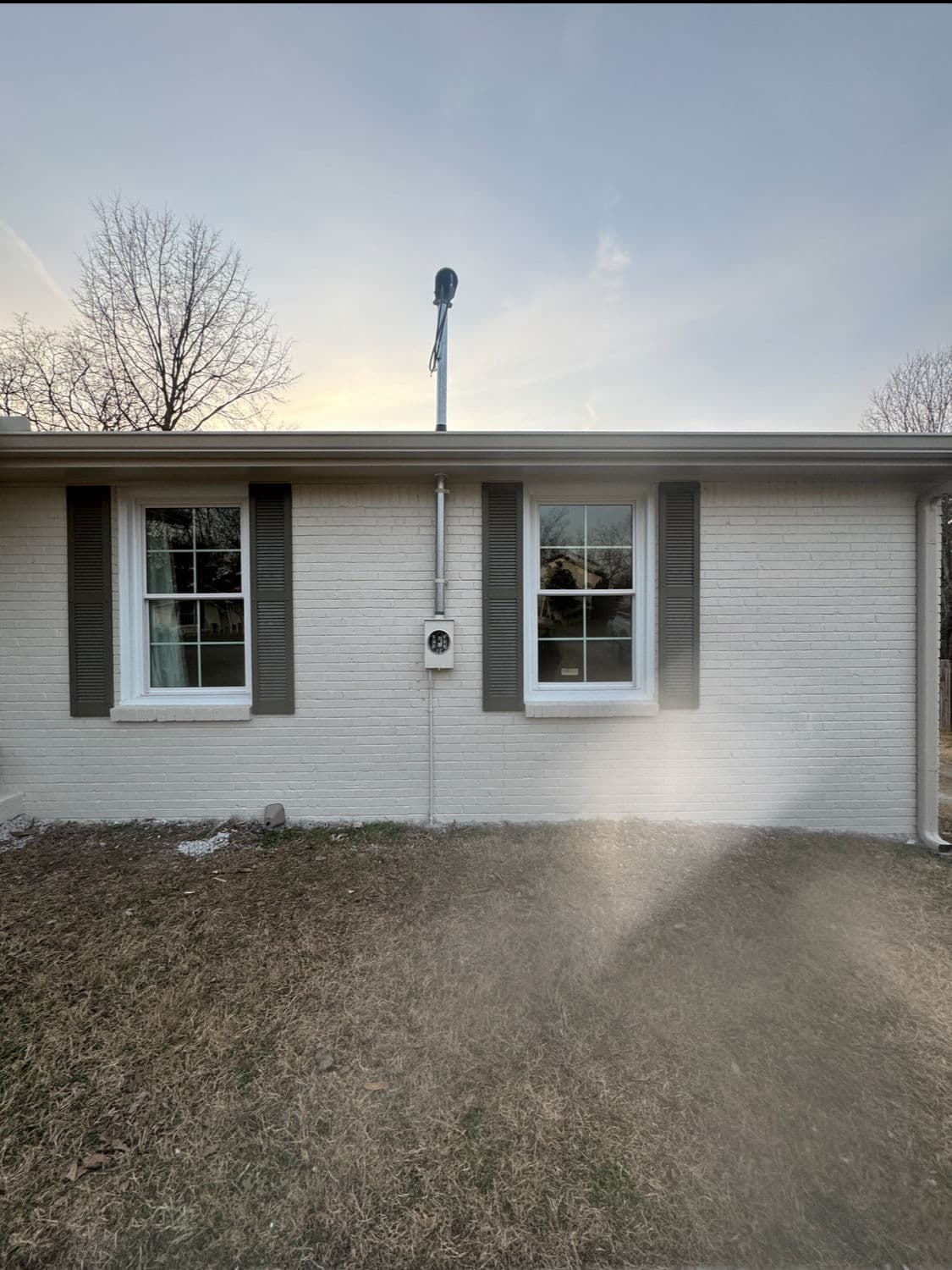 Two windows with gray shutters on a white brick house, grassy area in foreground.