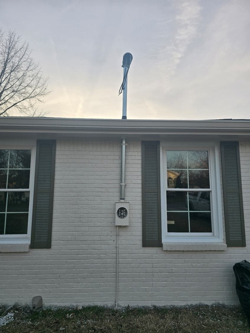 Utility pole with antenna on a brick house wall under a cloudy sky.