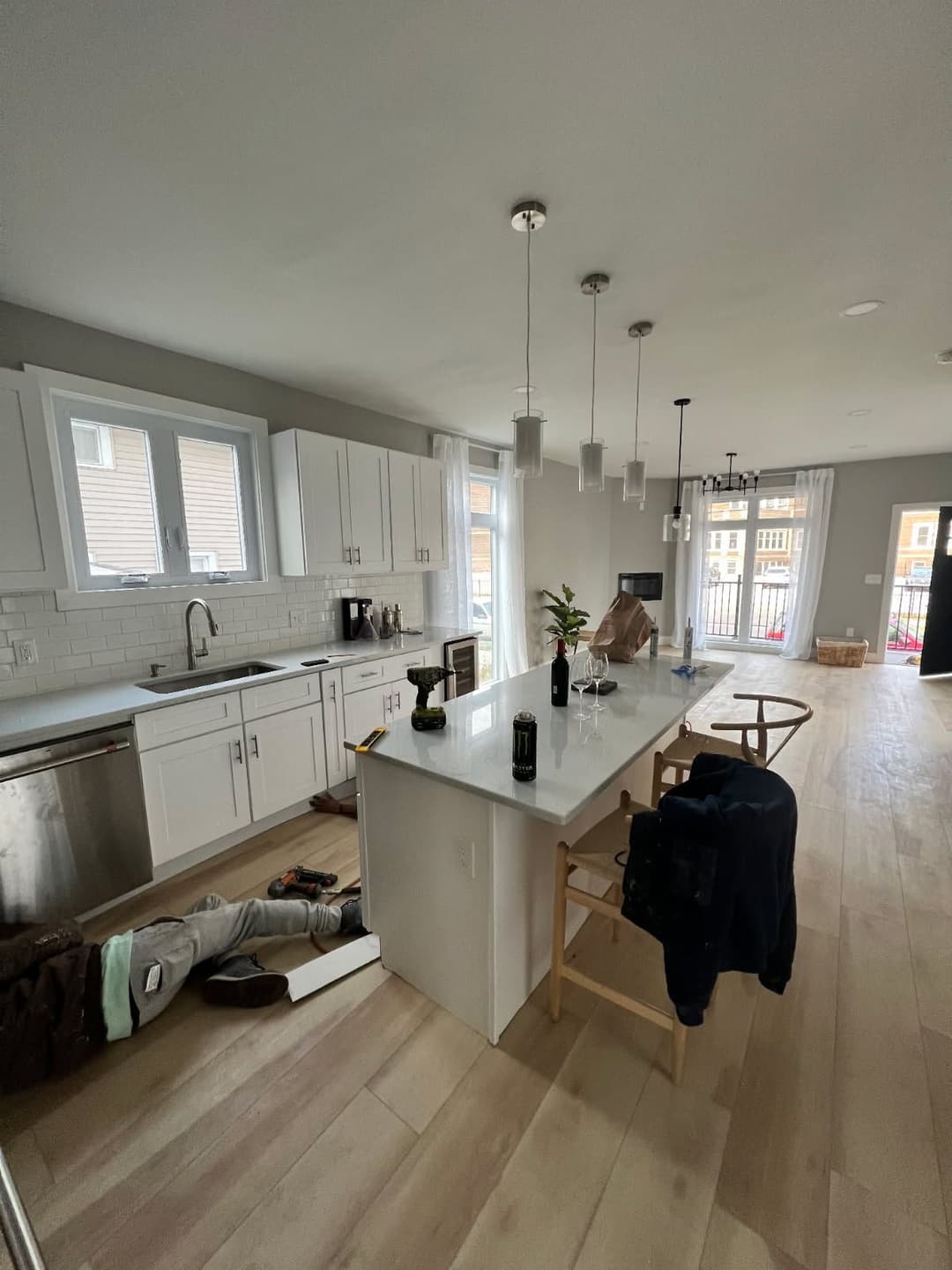 Modern kitchen with white cabinets and island, featuring a person working on the floor.