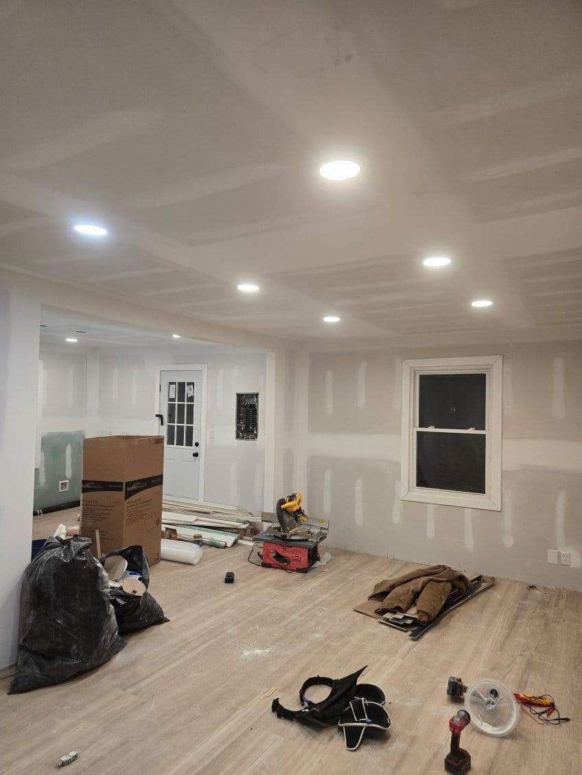 Renovated room with recessed lighting, drywall, and construction materials on the floor.