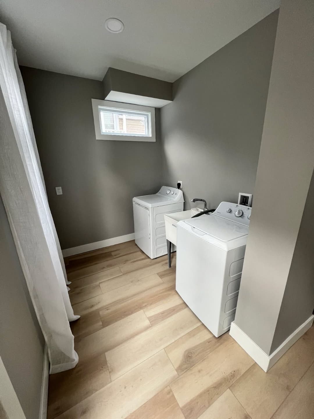 Laundry room featuring white washer and dryer against gray walls and light wood flooring.