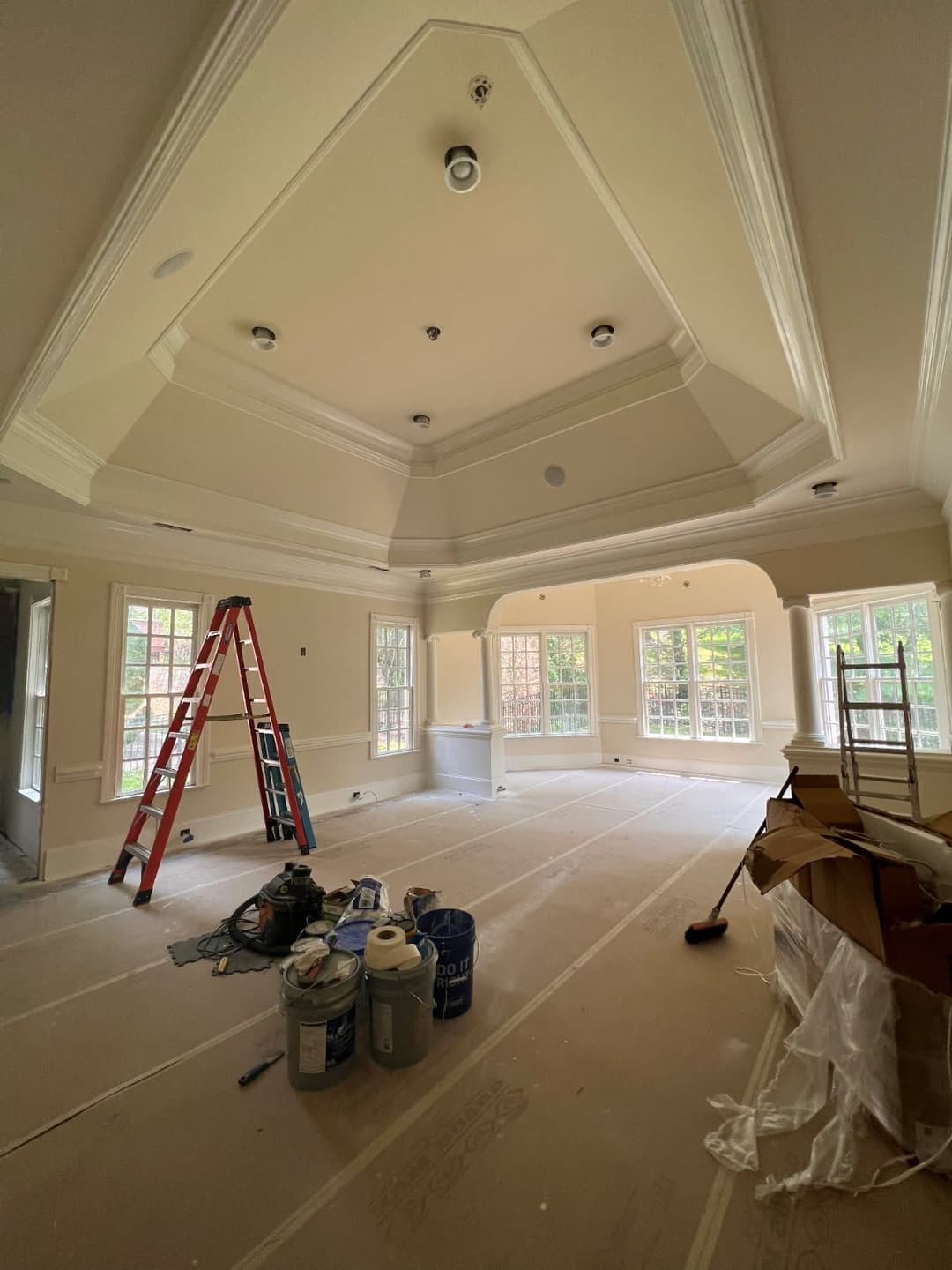 Renovated room with high ceiling, ladder, and paint supplies showcasing natural light.