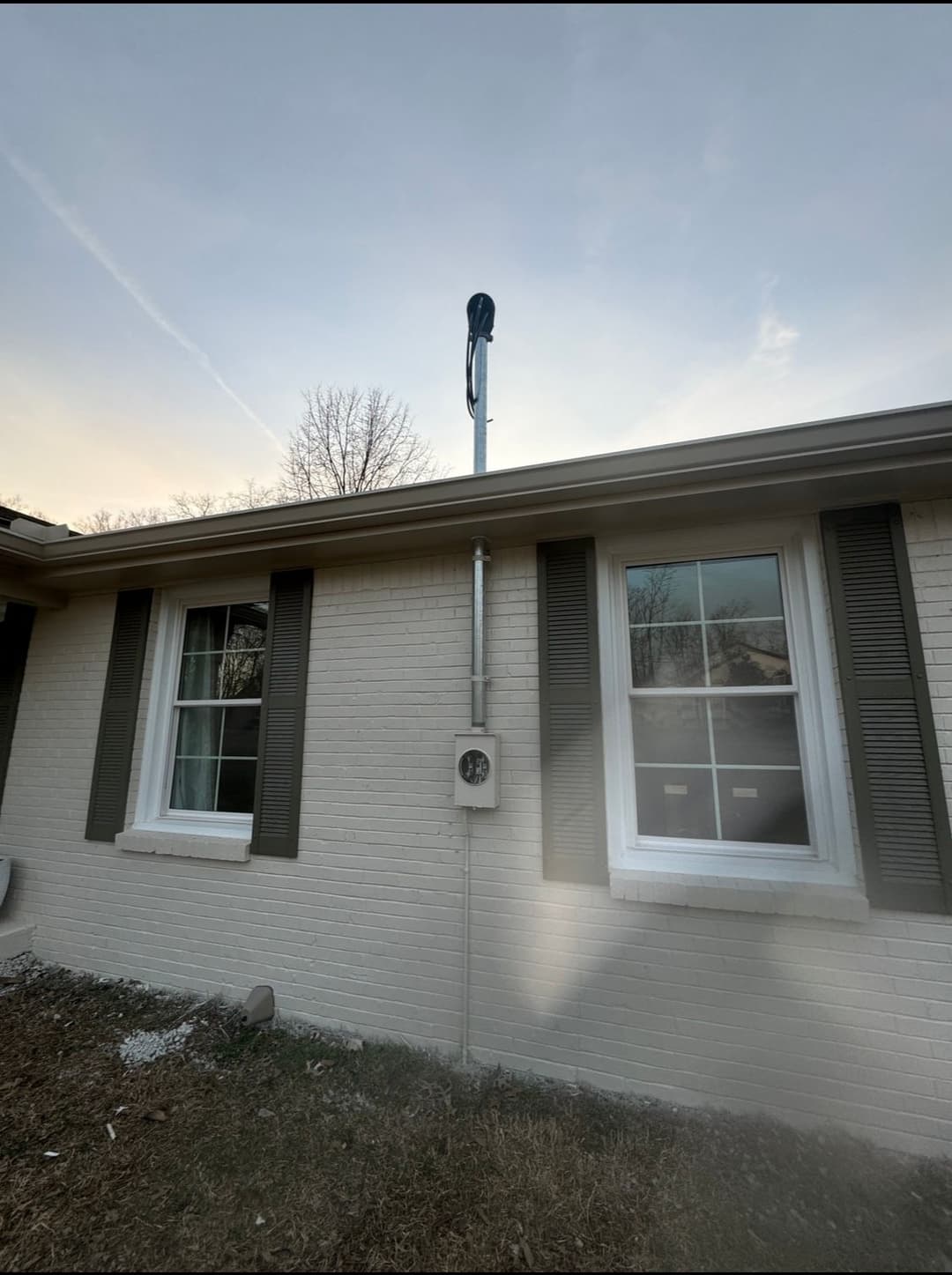 Wireless antenna mounted on a house roof with windows and a utility box below.