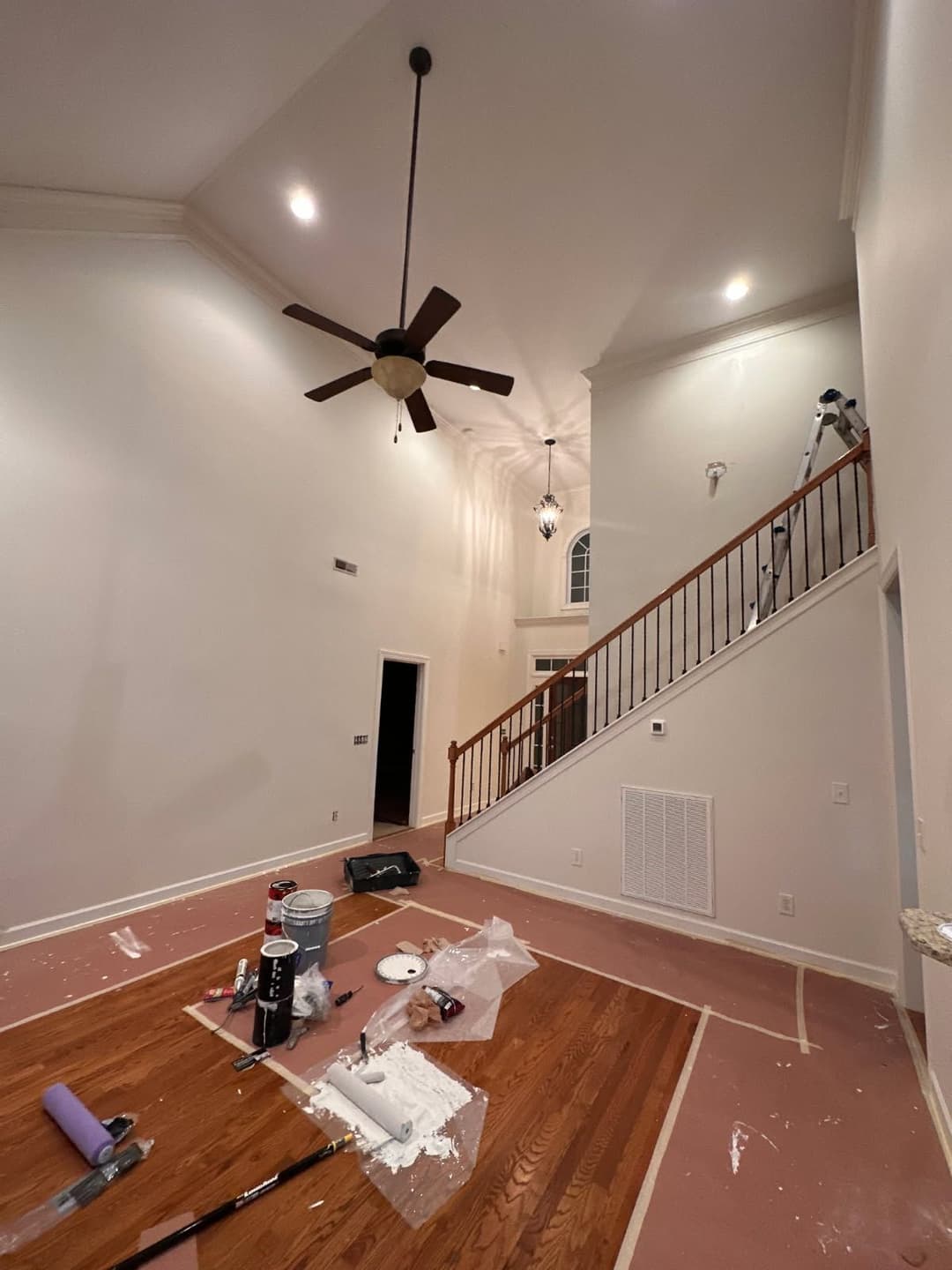 Living room under renovation, featuring a staircase, painter’s supplies, and white walls.