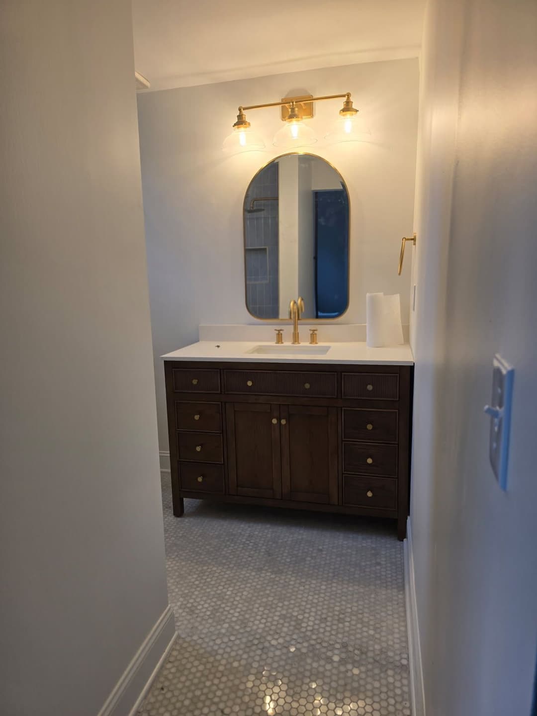 Modern bathroom interior with wooden vanity, gold fixtures, and hexagon tile flooring.