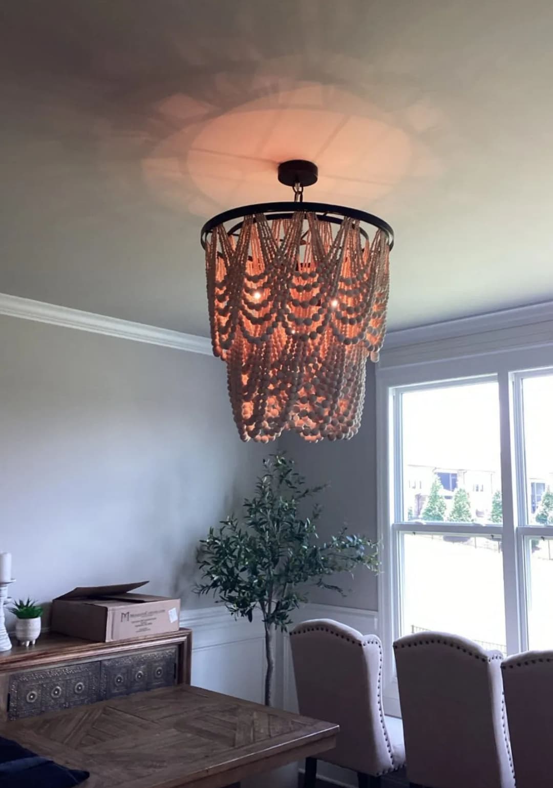 Elegant beaded chandelier hanging in a bright dining area with windows and greenery.