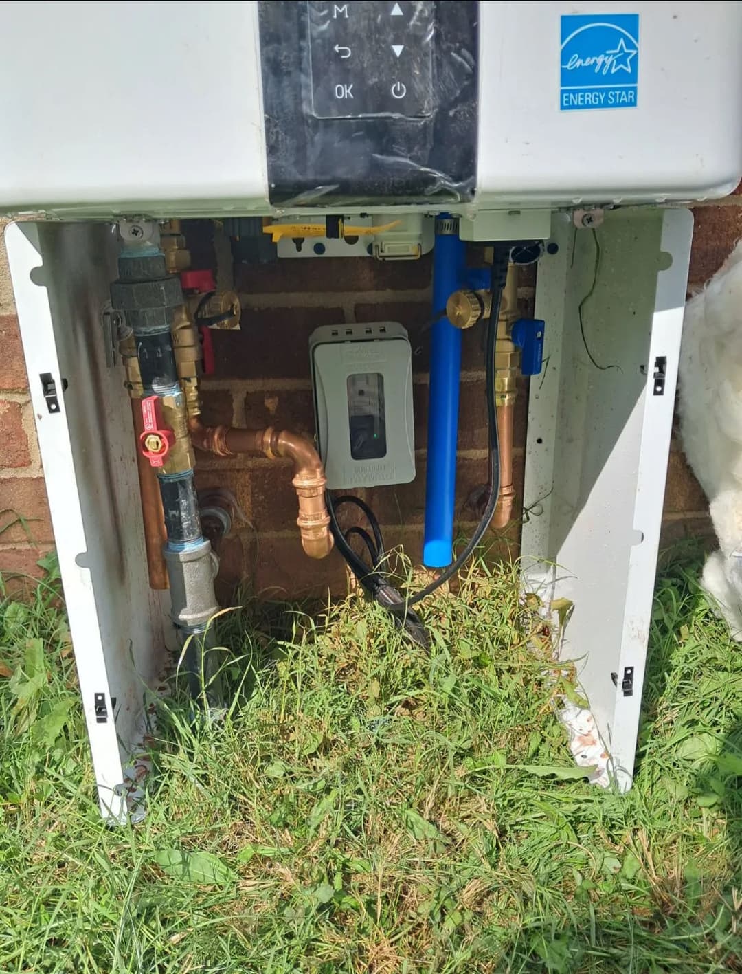 Outdoor tankless water heater installation showing pipes and connections in a grassy area.