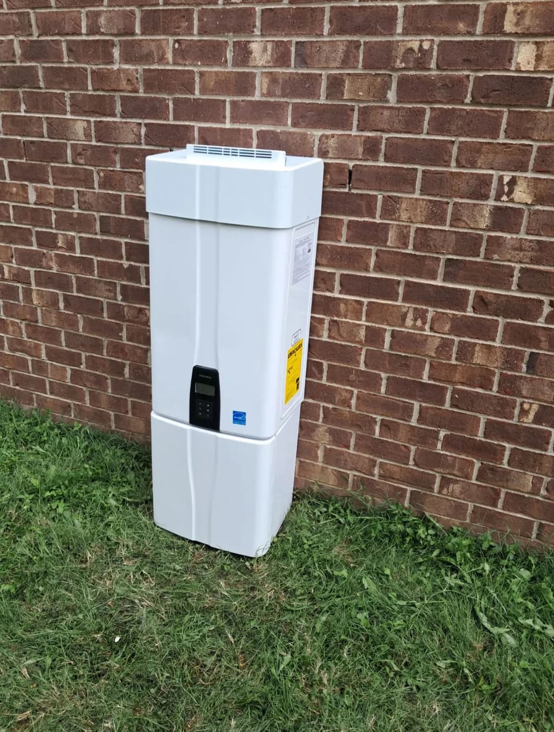 White air conditioning unit next to a brick wall, placed on grass.