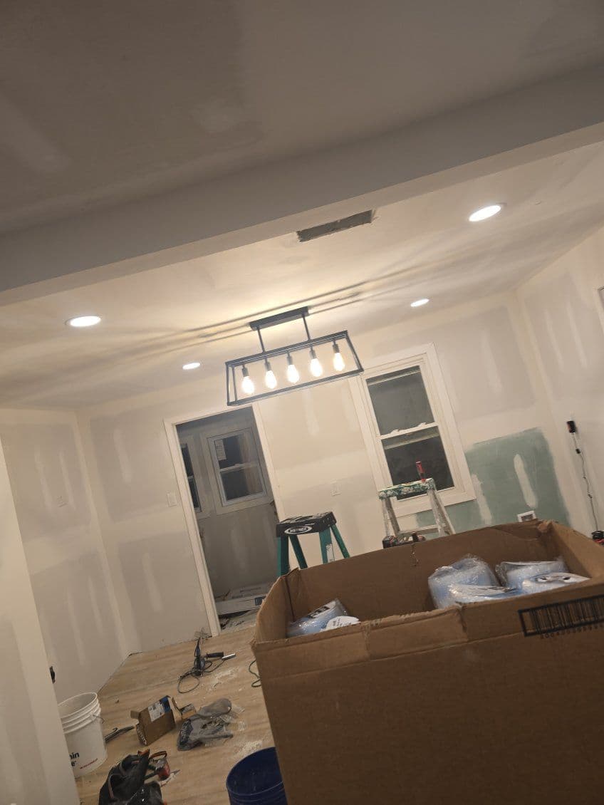 Renovated room showing drywall, new lighting, and a cardboard box of supplies.