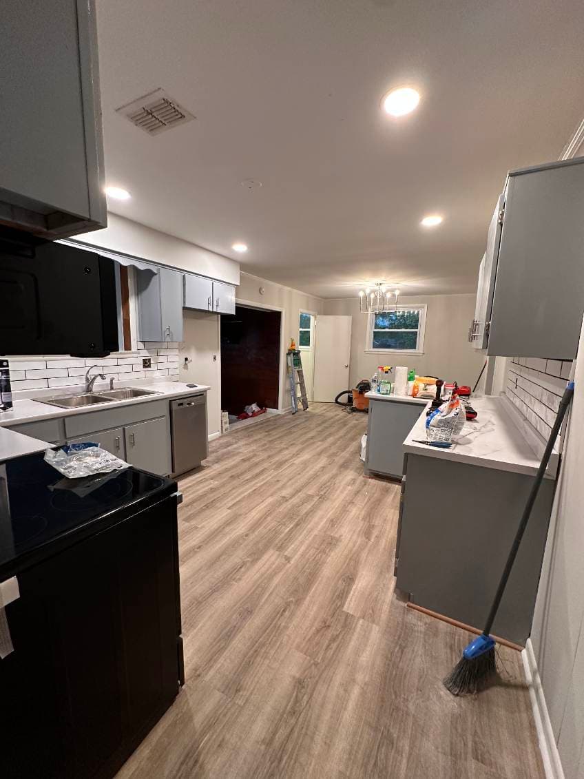 Modern kitchen with gray cabinets, black appliances, and wood-style flooring.