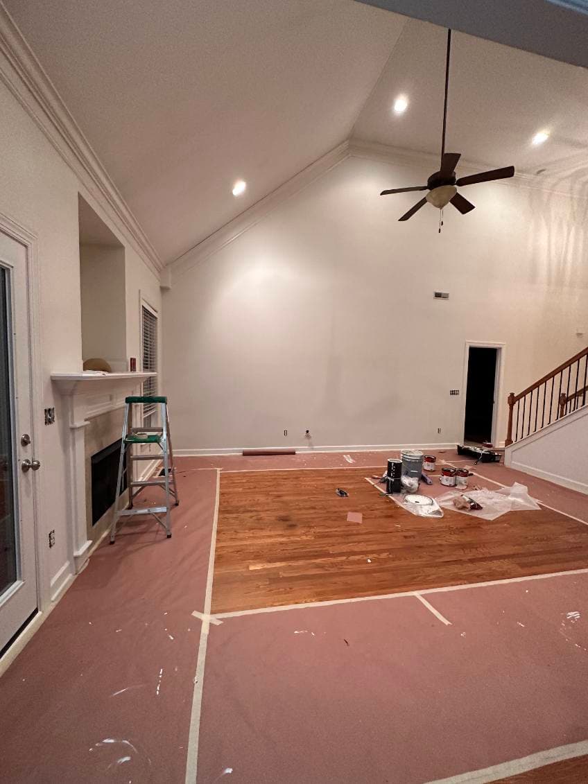 Renovated living room with wooden floor, paint supplies, and wall in preparation for painting.