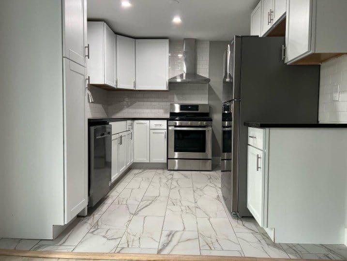 Modern kitchen with white cabinets, stainless steel appliances, and marble tile floor.