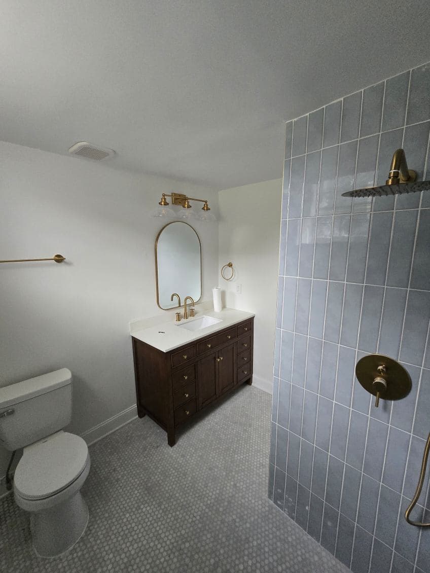 Modern bathroom with gold fixtures, wooden vanity, and blue tiled shower.